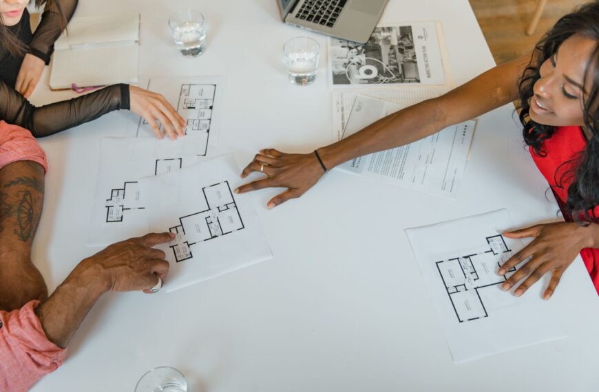 Several people around a table reviewing architectural floor plans, representing pooled investment in a real estate syndication